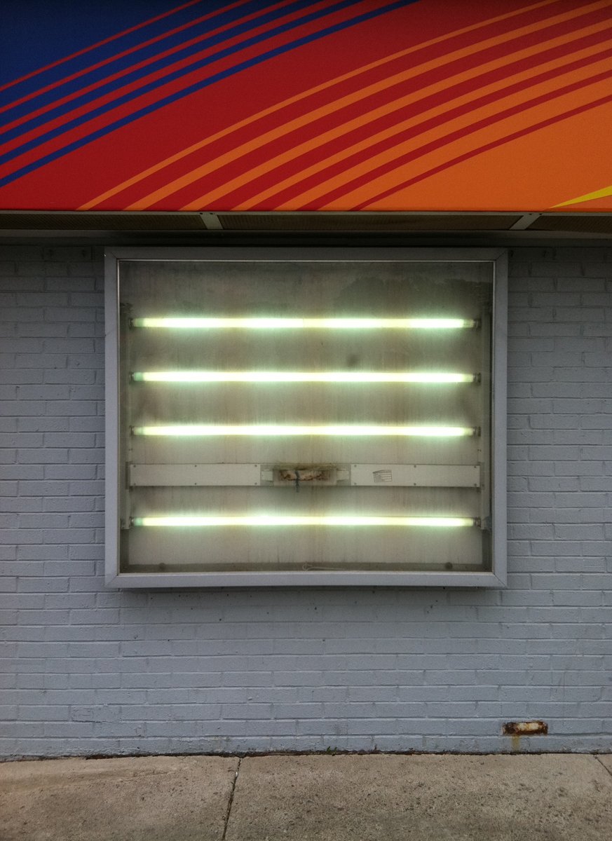 Four bare fluorescent lightbulbs in a metal box on a grey painted brick wall.