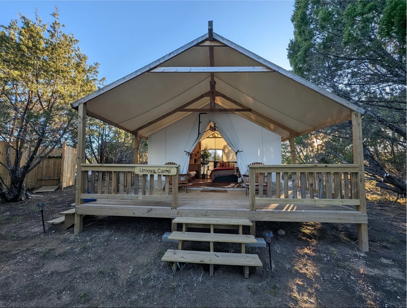 Luxurious glamping tent illuminated at dusk with cozy interior, set in a scenic nature landscape with trees and rocks.