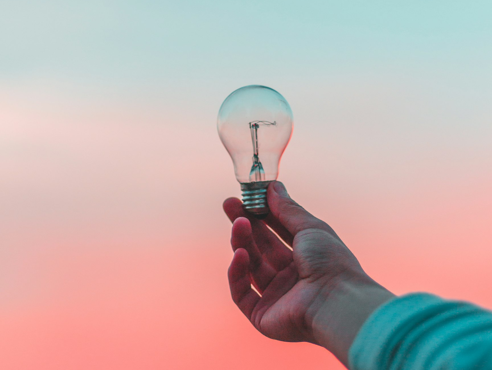 Mano sosteniendo una bombilla incandescente contra un cielo degradado al atardecer, concepto de ideas e innovación