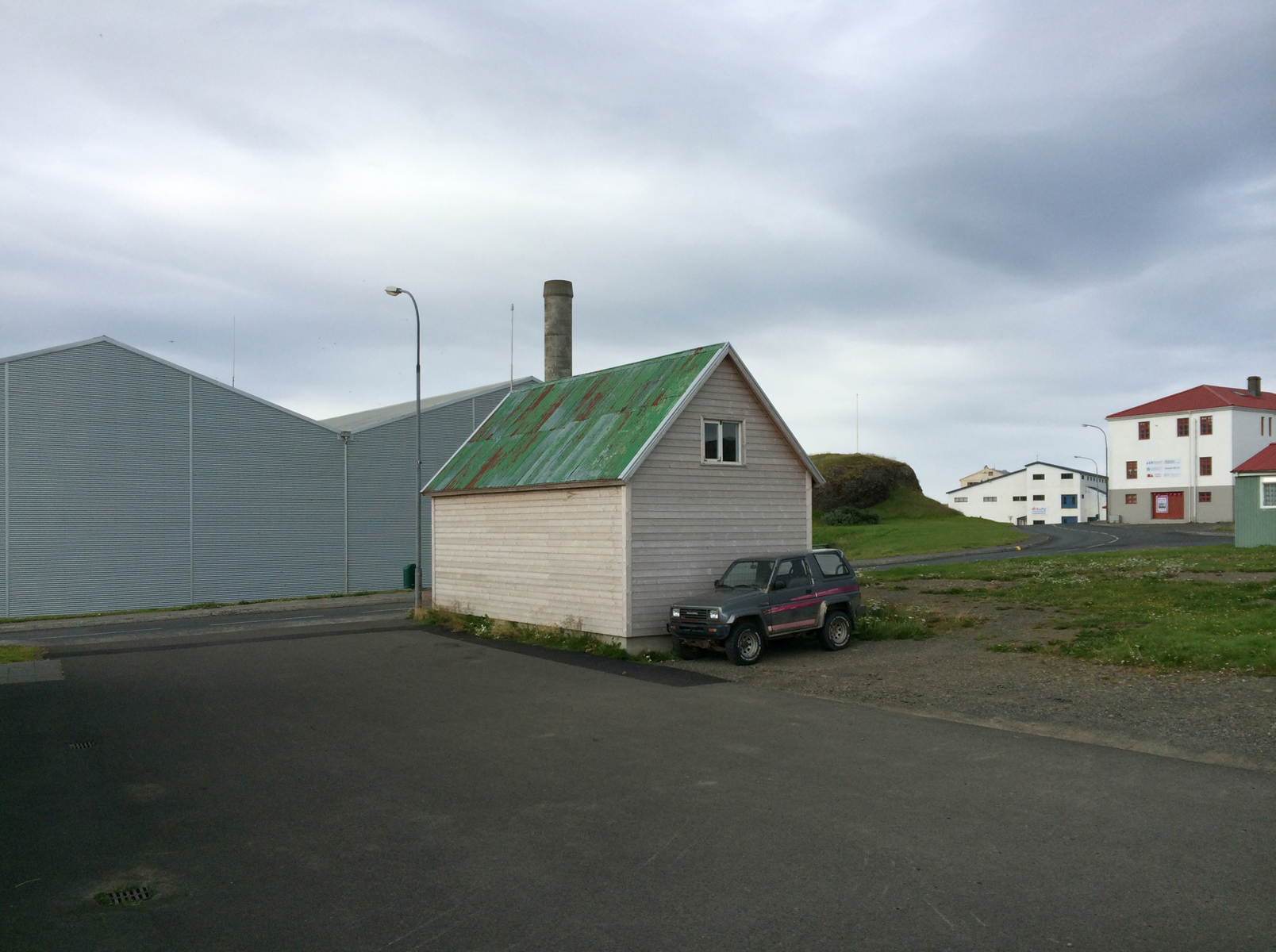 In expanse of asphalt and grey sky, a small building with a green metal roof.