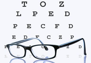 Gafas negras frente a tabla optométrica con letras de diferentes tamaños.