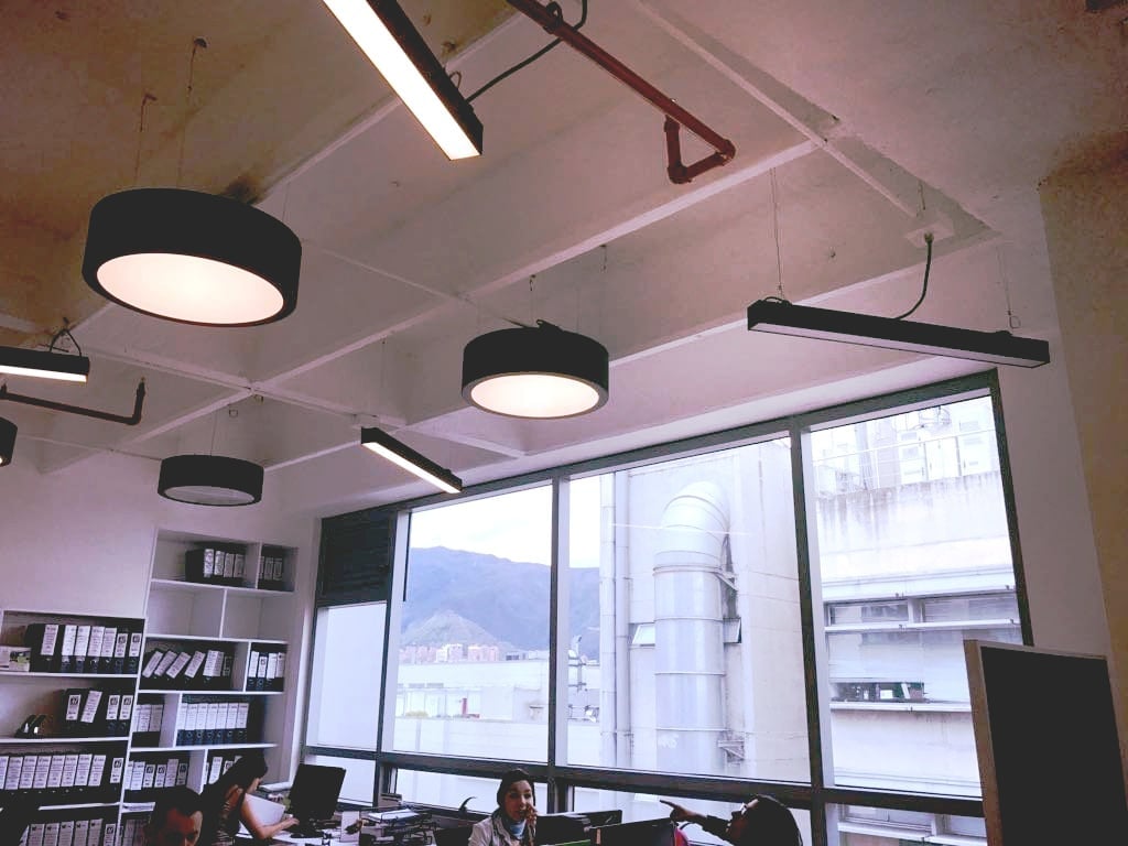 Oficina moderna con lámparas de techo, grandes ventanales y estanterías llenas de archivadores.