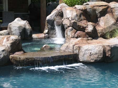 Natural rock waterfall flowing into a clear blue pool surrounded by large boulders.