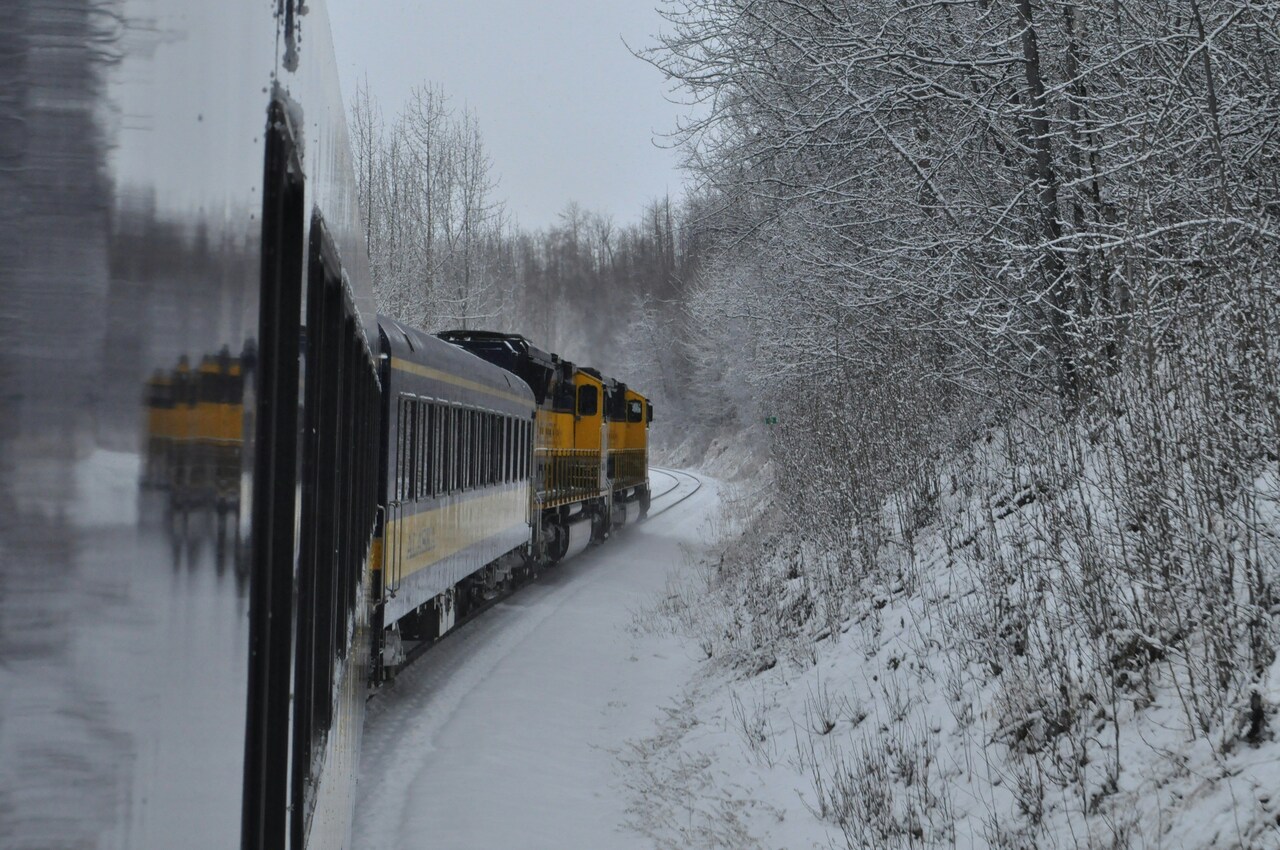 Tren amarillo y negro avanzando por vías cubiertas de nieve en un paisaje invernal con árboles sin hojas. Tren amarillo y negro avanzando por vías cubiertas de nieve en un paisaje invernal con árboles sin hojas.