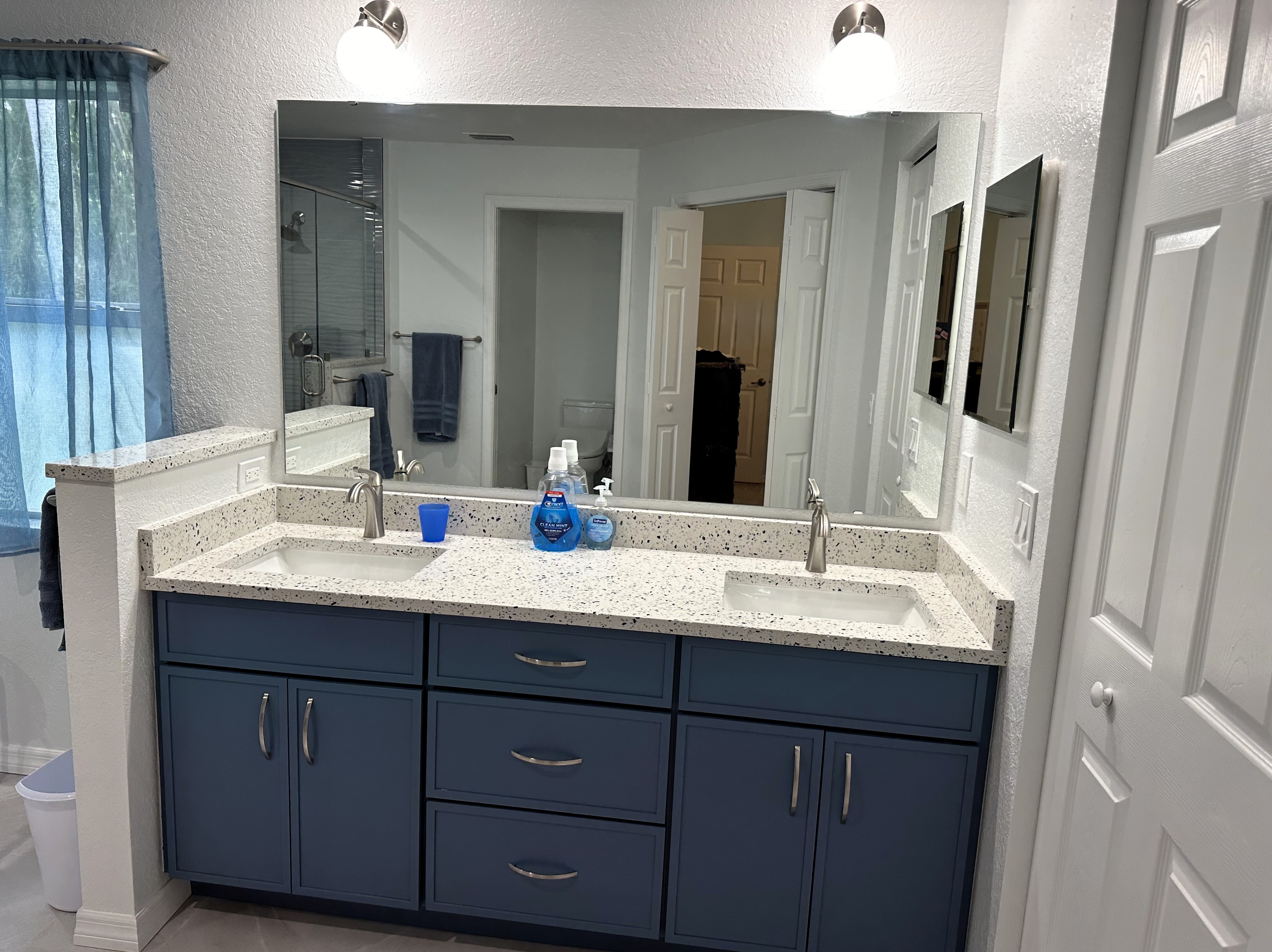 This well-crafted double vanity combines the calming hue of Lakeshore Blue with sleek shaker-style doors, recycled glass quartz countertops, and a matching 4" backsplash to create a beautifully framed, harmonious space.