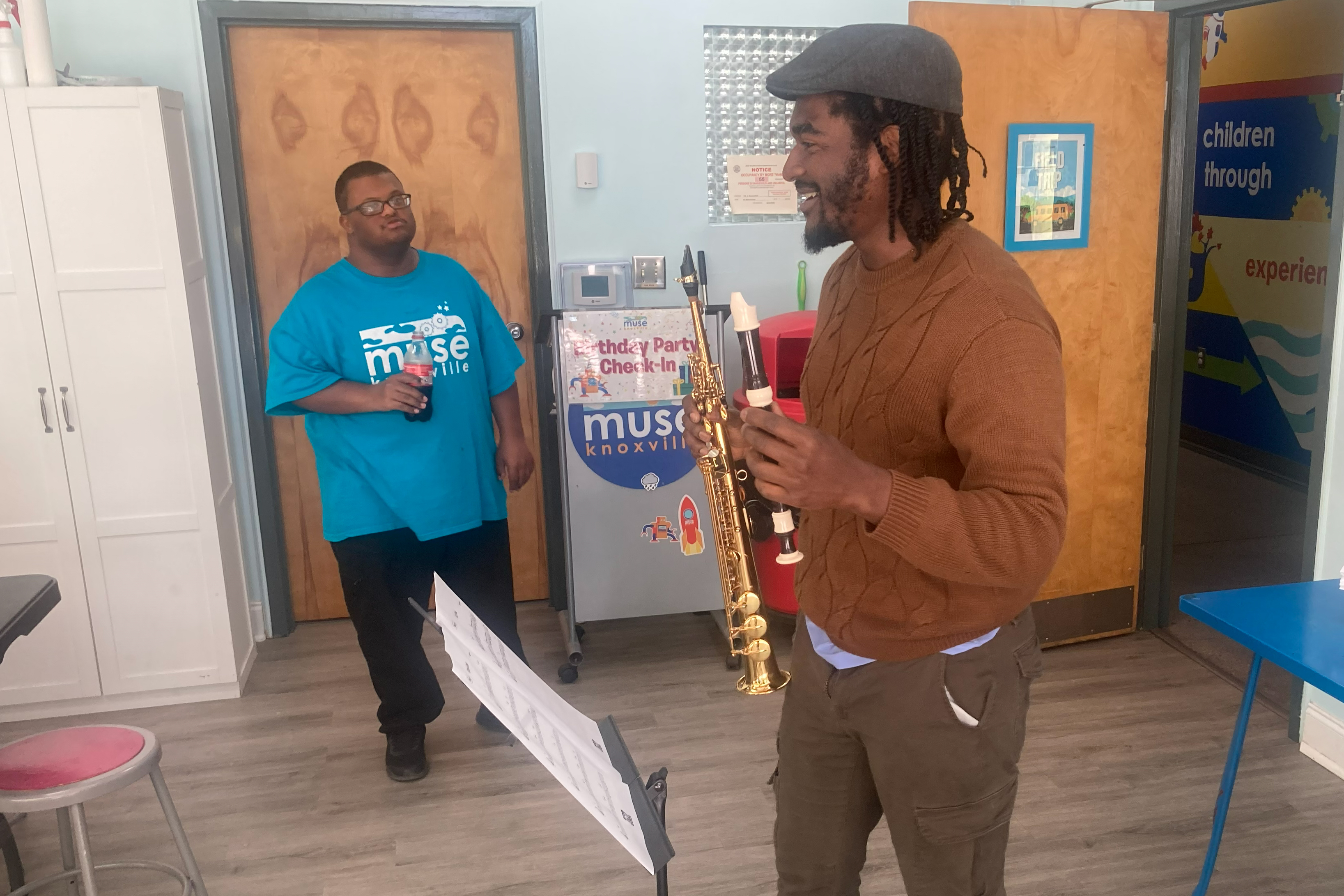 Cozy music room with double bass, acoustic guitar, keyboard, and a blackboard with 'Jazz' written on it, surrounded by plants and books.