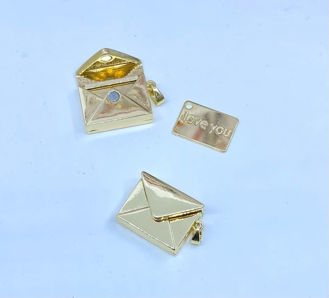 Colgante dorado con forma de sobre, abierto mostrando un interior brillante, junto a una placa que dice 'love you'. Colgante dorado con forma de sobre, abierto mostrando un interior brillante, junto a una placa que dice 'love you'.