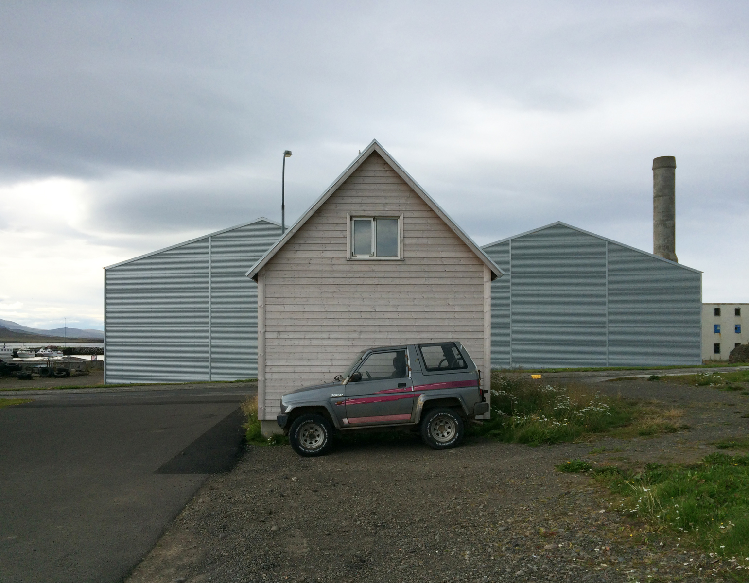A small grey SUV parked in front of the peaked gable end of a small building.