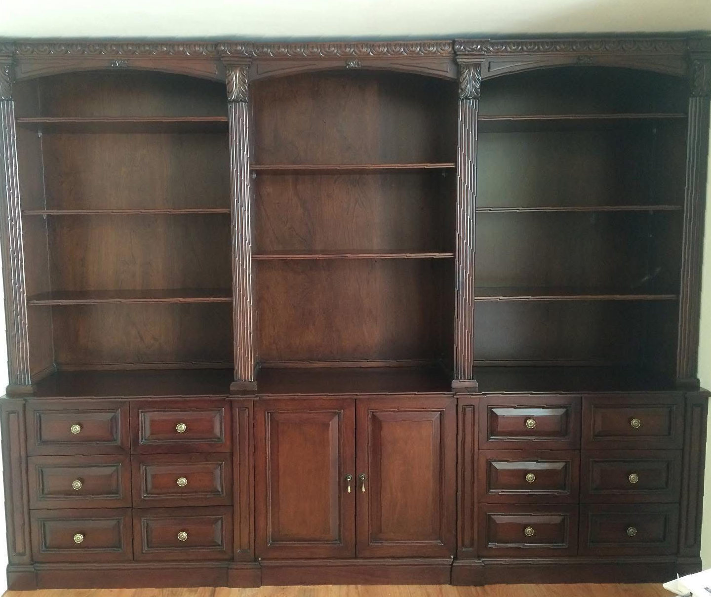 Cocina moderna con isla central de madera clara, taburetes blancos, lámparas colgantes metálicas y estantes iluminados.