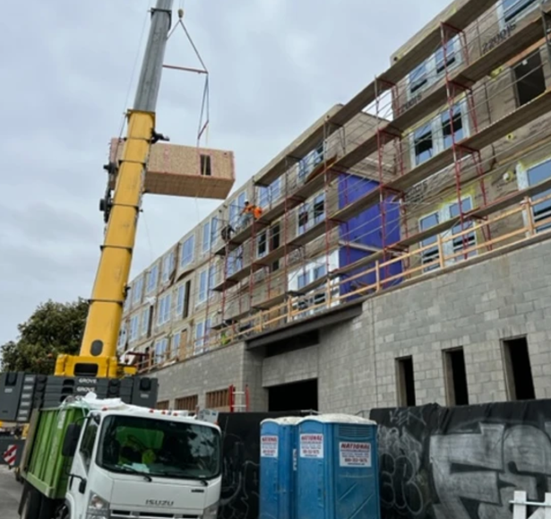 Woman in a modern office setting, holding a smartphone, with plants and open books on a wooden desk, suggesting productivity and style.