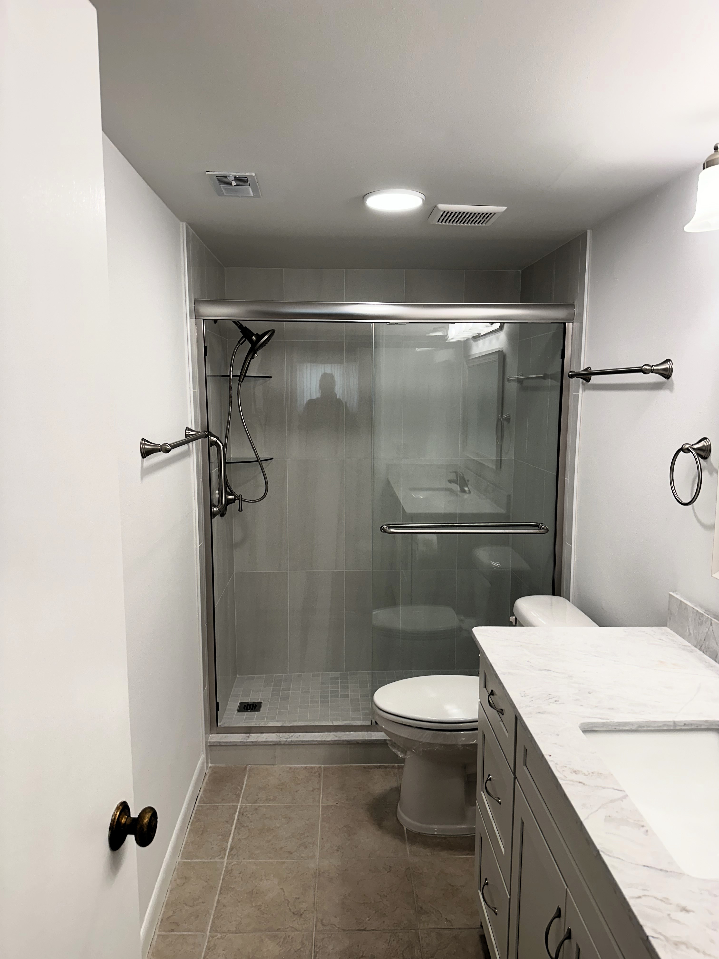 Beautifully tiled walk-in shower featuring polished 12x24 wall tile, matching 2x2 matte finish shower floor, and enhanced with semi-frameless by-passing shower doors in brush nickel.
