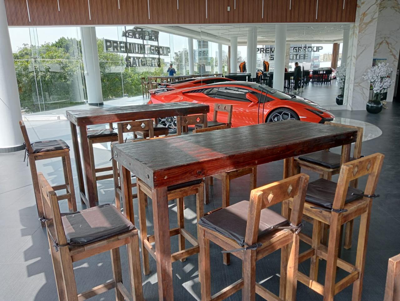 Mesa de madera con sillas altas frente a un auto deportivo rojo en showroom moderno. Mesa de madera con sillas altas frente a un auto deportivo rojo en showroom moderno.