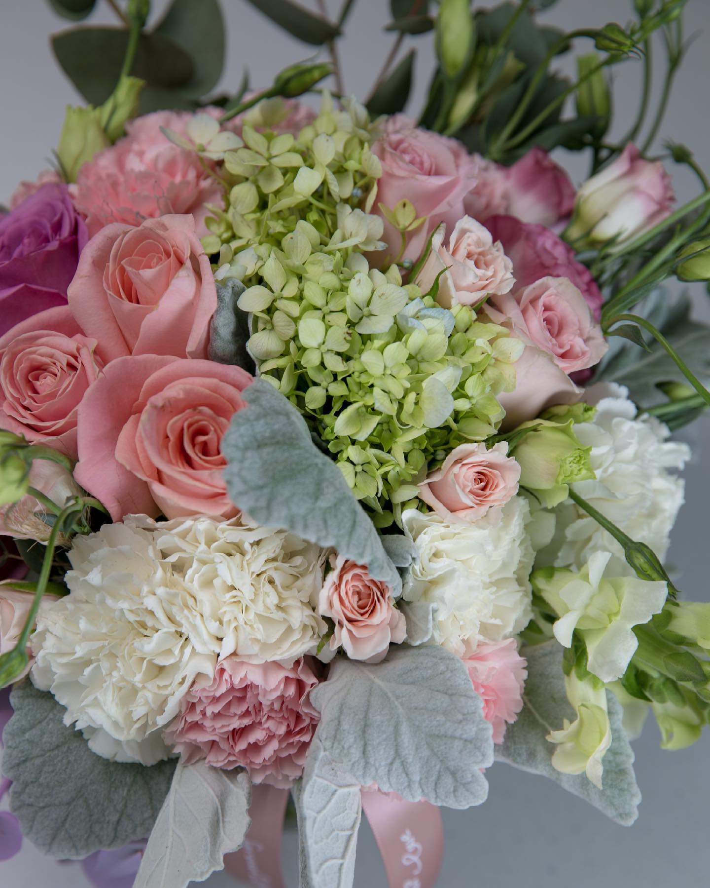 Arreglo floral con rosas rosadas y margaritas en un jarrón sobre una mesa cerca de una ventana.