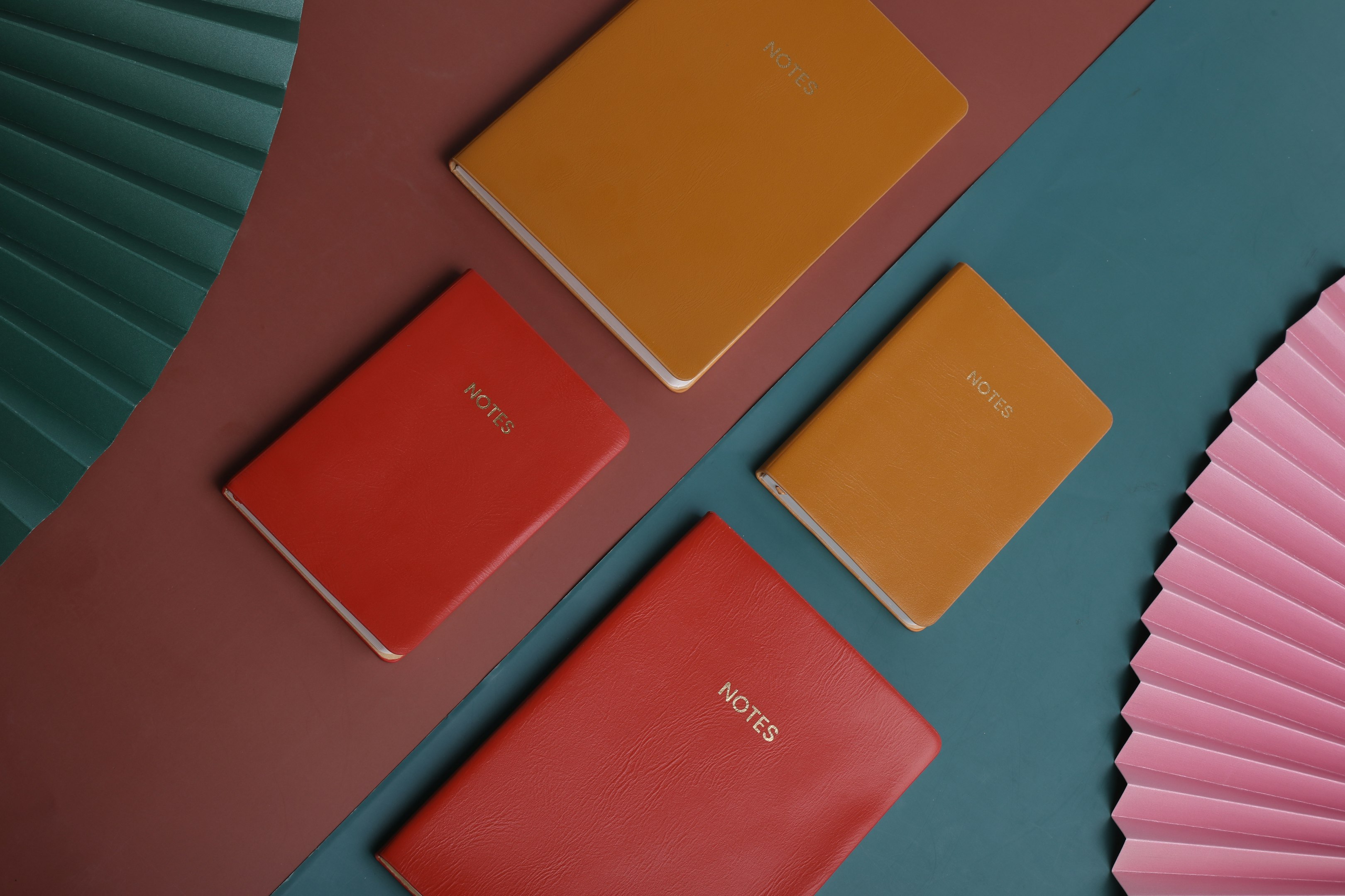 tres cuadernos de diferentes colores junto a un ventilador rosa
