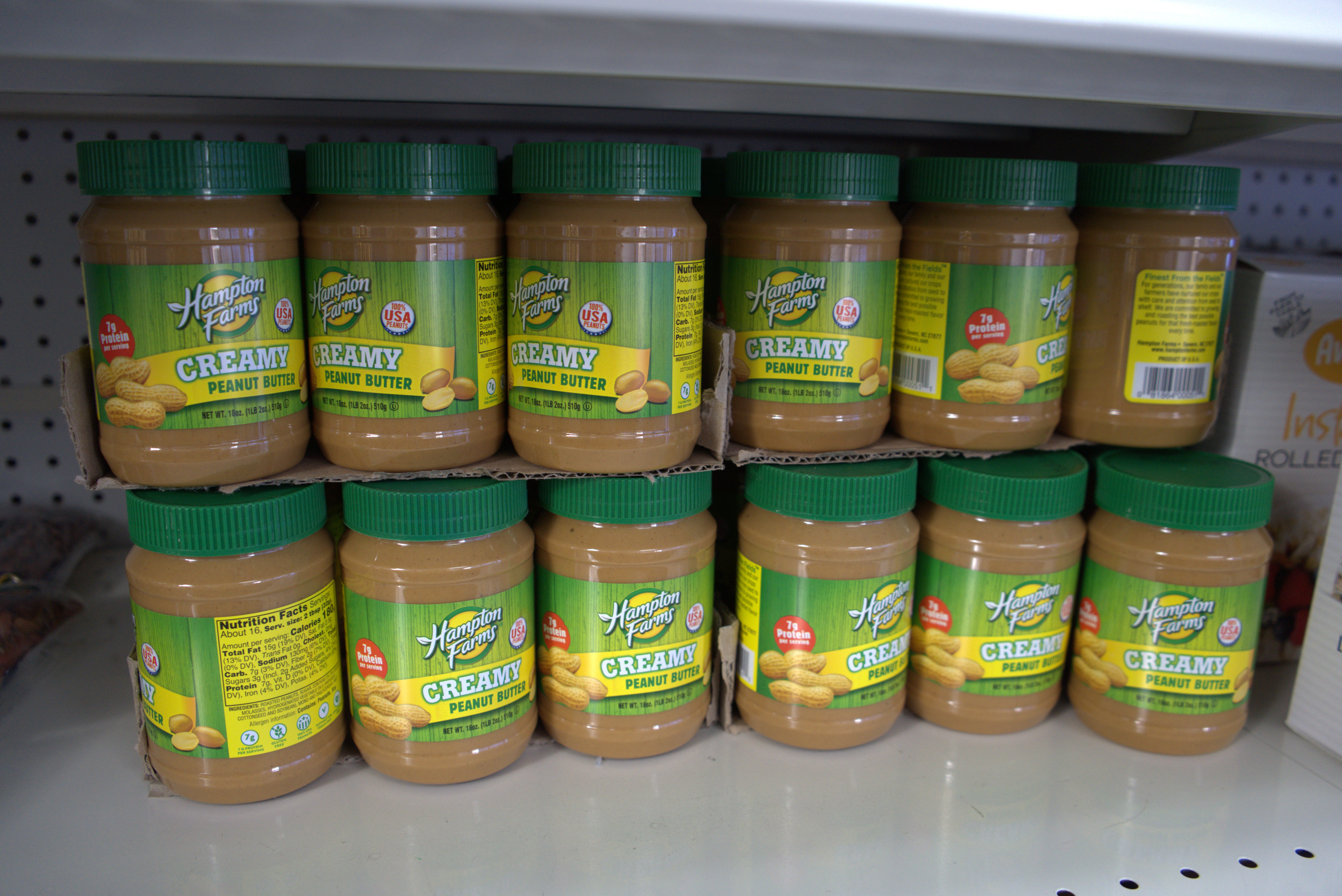 Assorted grocery items on a store shelf including pasta, cheese, milk, fruits, vegetables, juice, and packaged food products in a bright supermarket aisle.