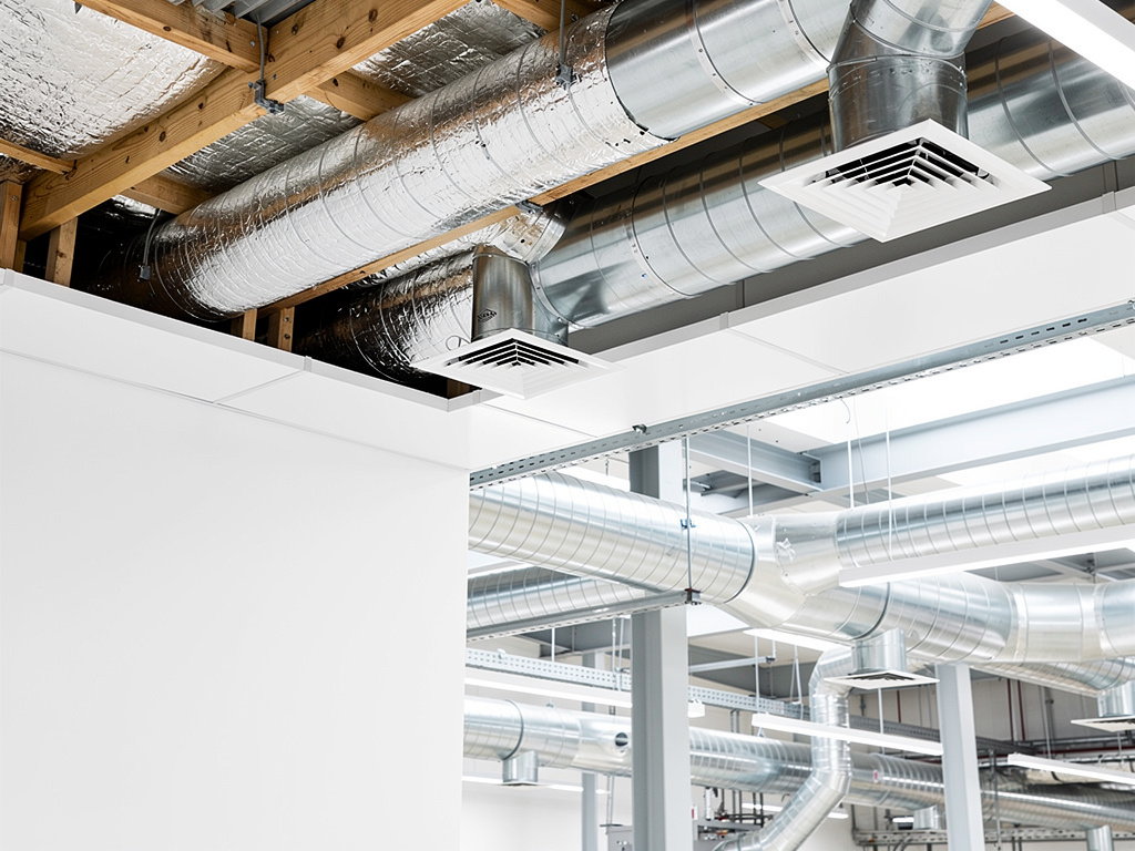 Conductos metálicos de ventilación HVAC en techo industrial con rejillas de aire acondicionado