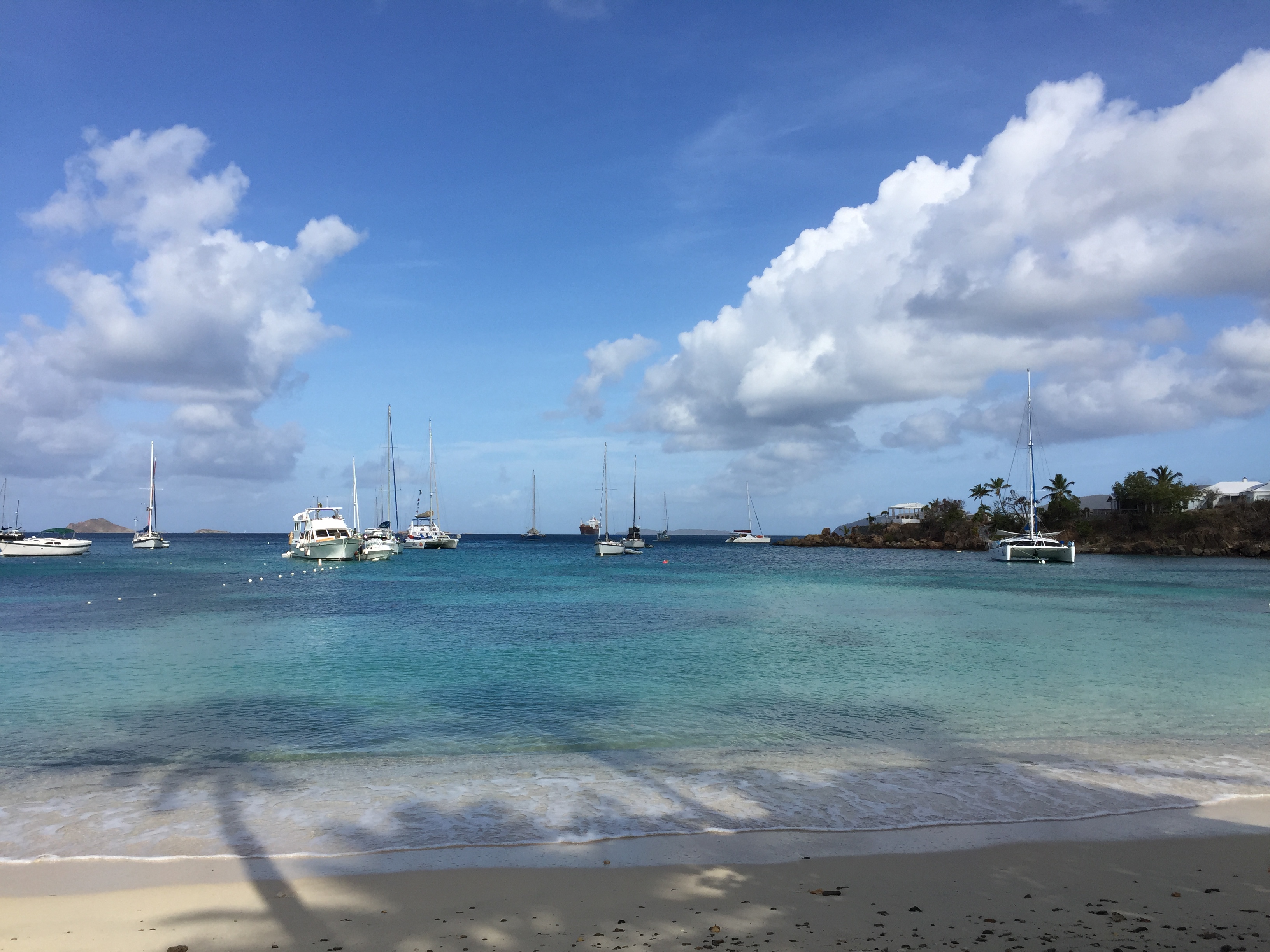 Luxury beachfront villas with palm trees on a tropical island, turquoise ocean water, and a person in a small boat, serene vacation destination.