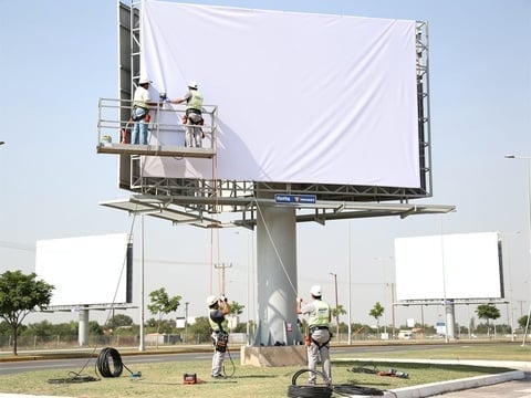 Técnicos instalando una lona blanca en un gran espectacular publicitario exterior