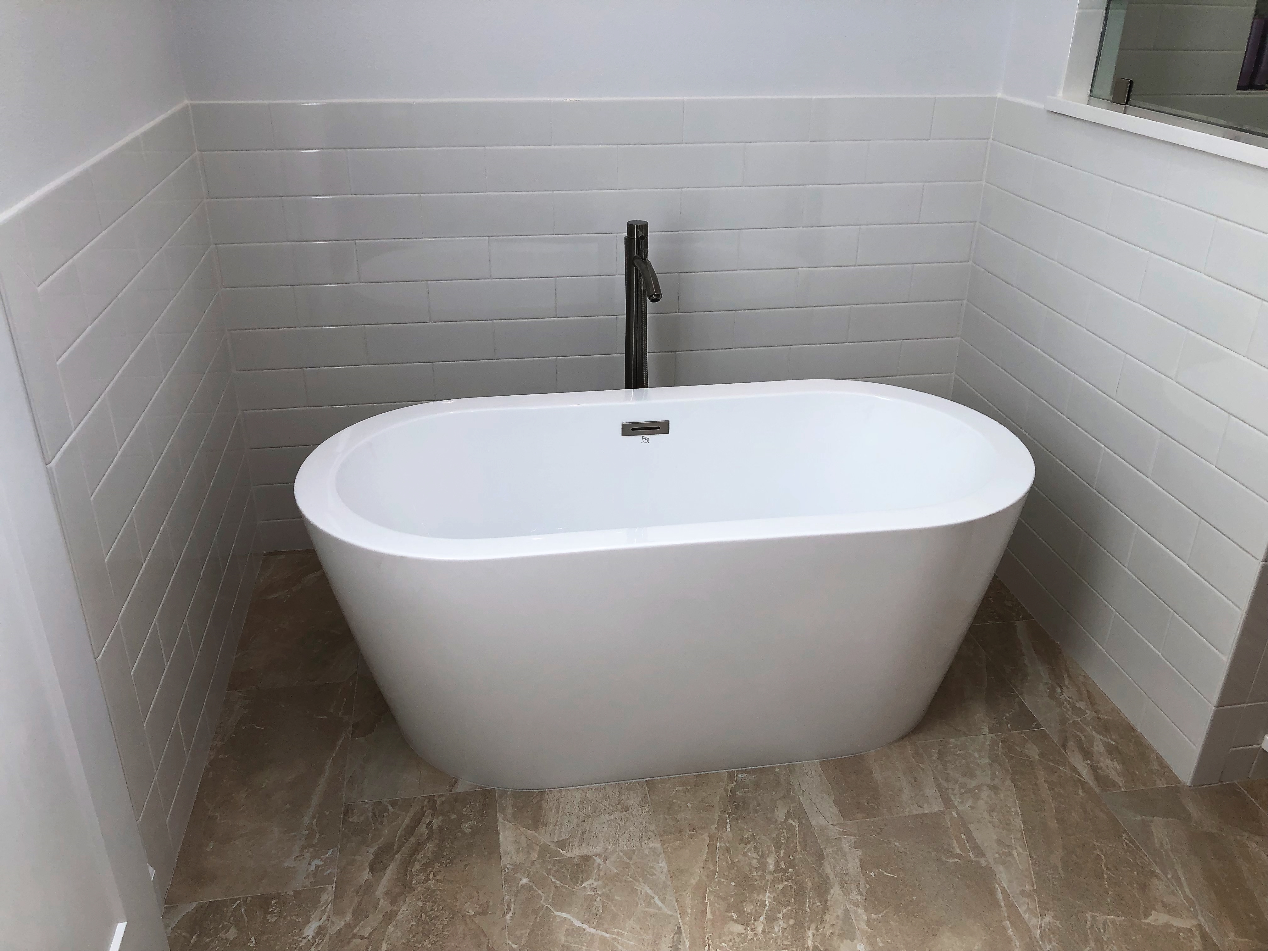 Free standing tub with white subway tile surround and Flint Ivory Tile flooring.