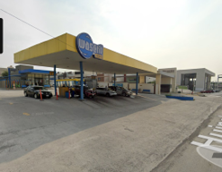 Outdoor car wash facility with yellow and blue signage, several cars being washed, and pavement marking.