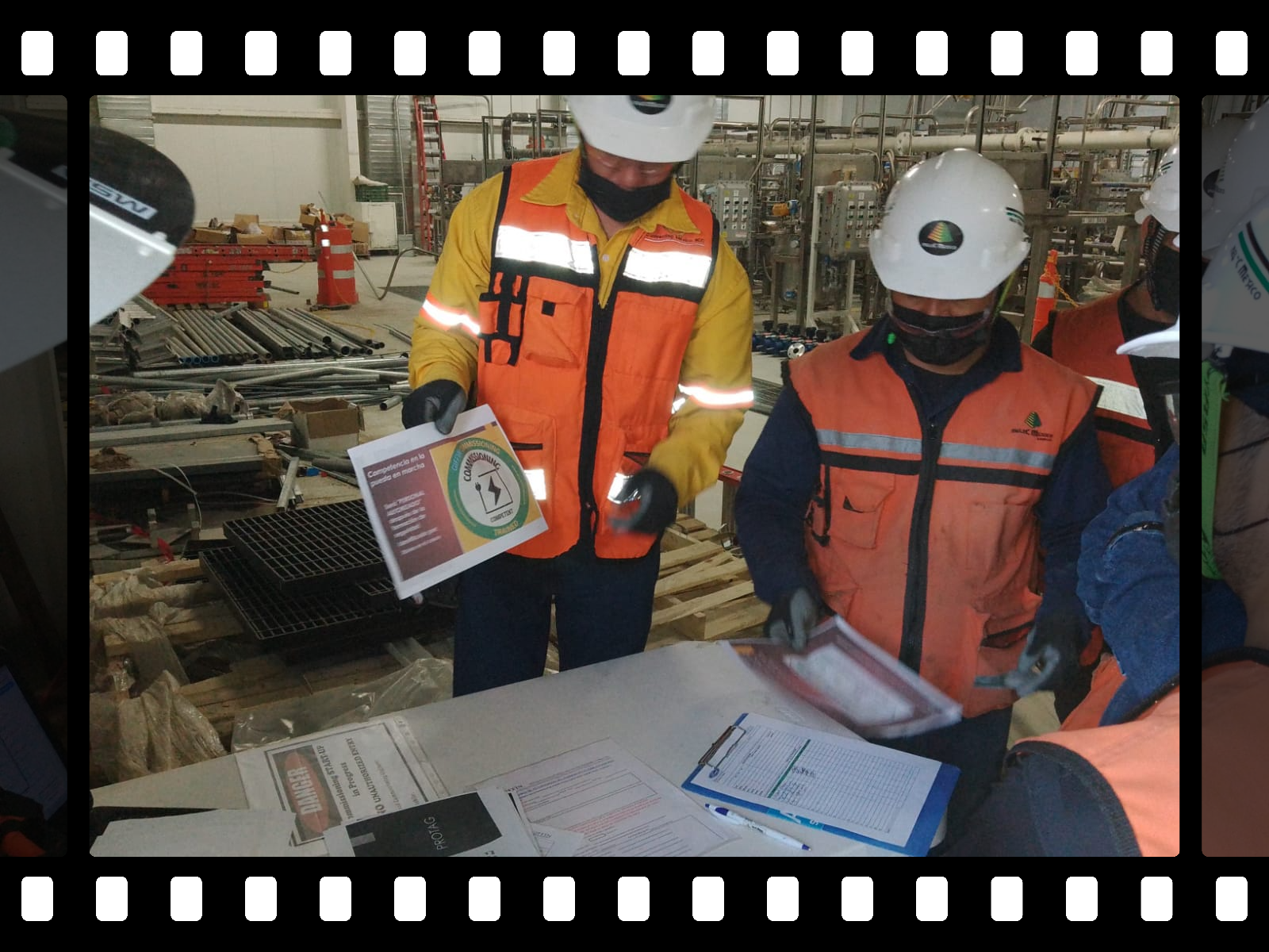 Dos trabajadores con cascos y chalecos en una planta industrial moderna, uno usando una computadora portátil y el otro supervisando el entorno.