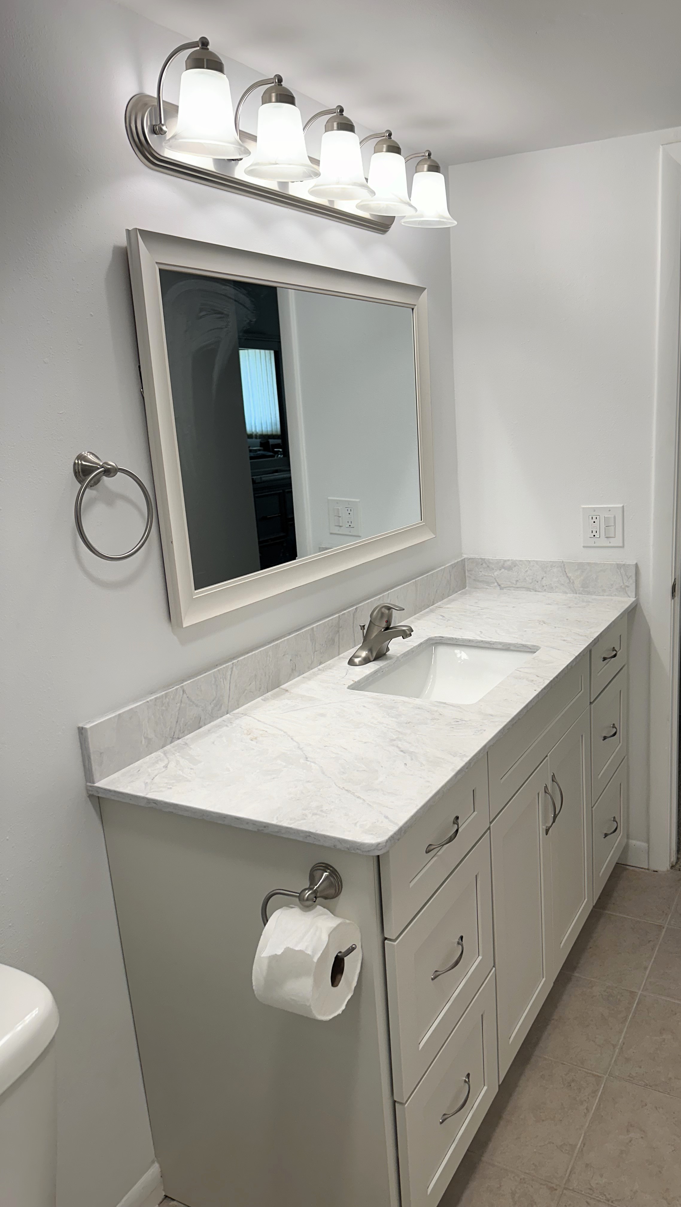 Charming vanity showcasing semi-custom maple wood cabinetry painted Steam, complemented by a quartz countertop with matching 4" backsplash, and finished with satin nickel handles.