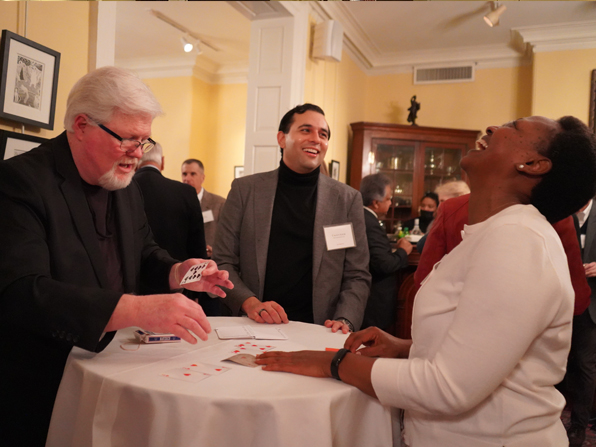Two guests standing at a table enjoying a card trick performed by Chuck. Two guests standing at a table enjoying a card trick performed by Chuck.
