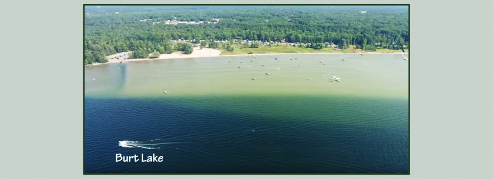 Aerial view of Burt Lake with boats scattered on the water and dense forest in the background.