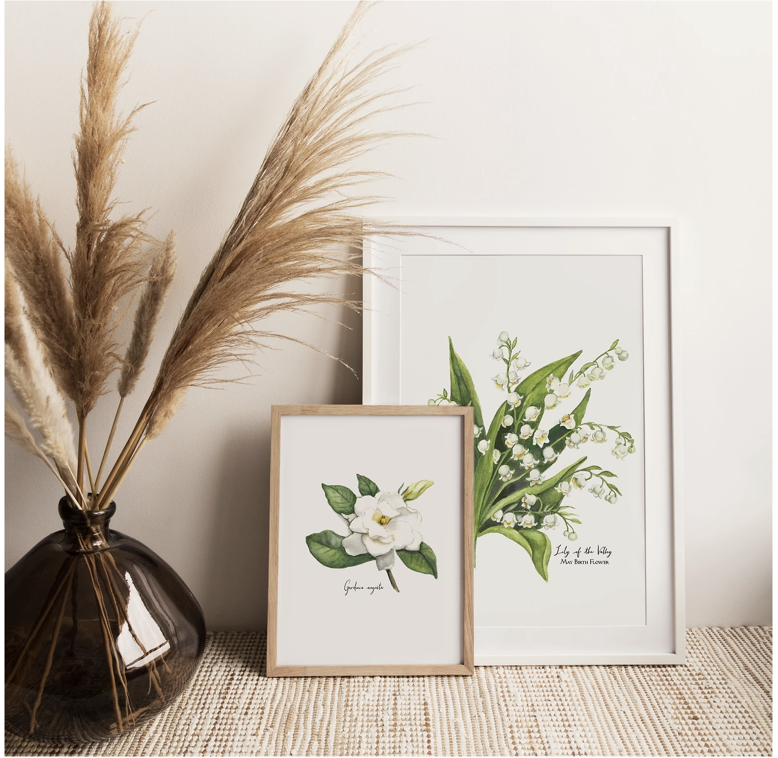 Decorative framed botanical prints of lily of the valley and gardenia in a cozy setting with pampas grass in a dark vase.
