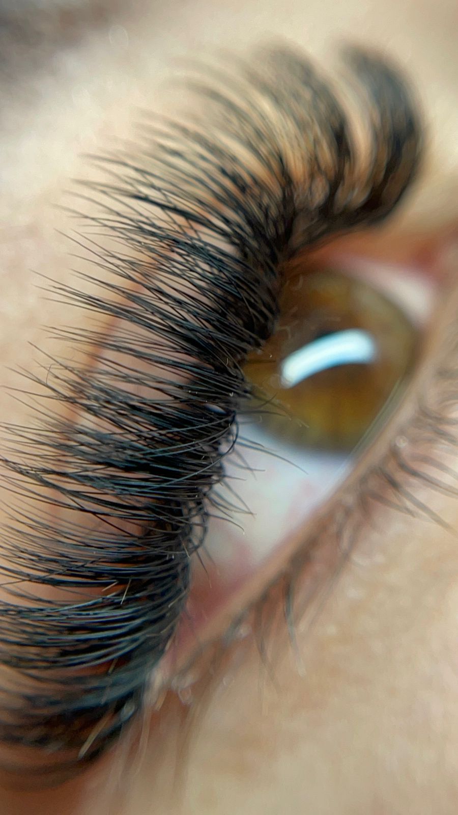 Mujer con maquillaje brillante y uñas rosas, mostrando una tez impecable y sombra de ojos dorada.