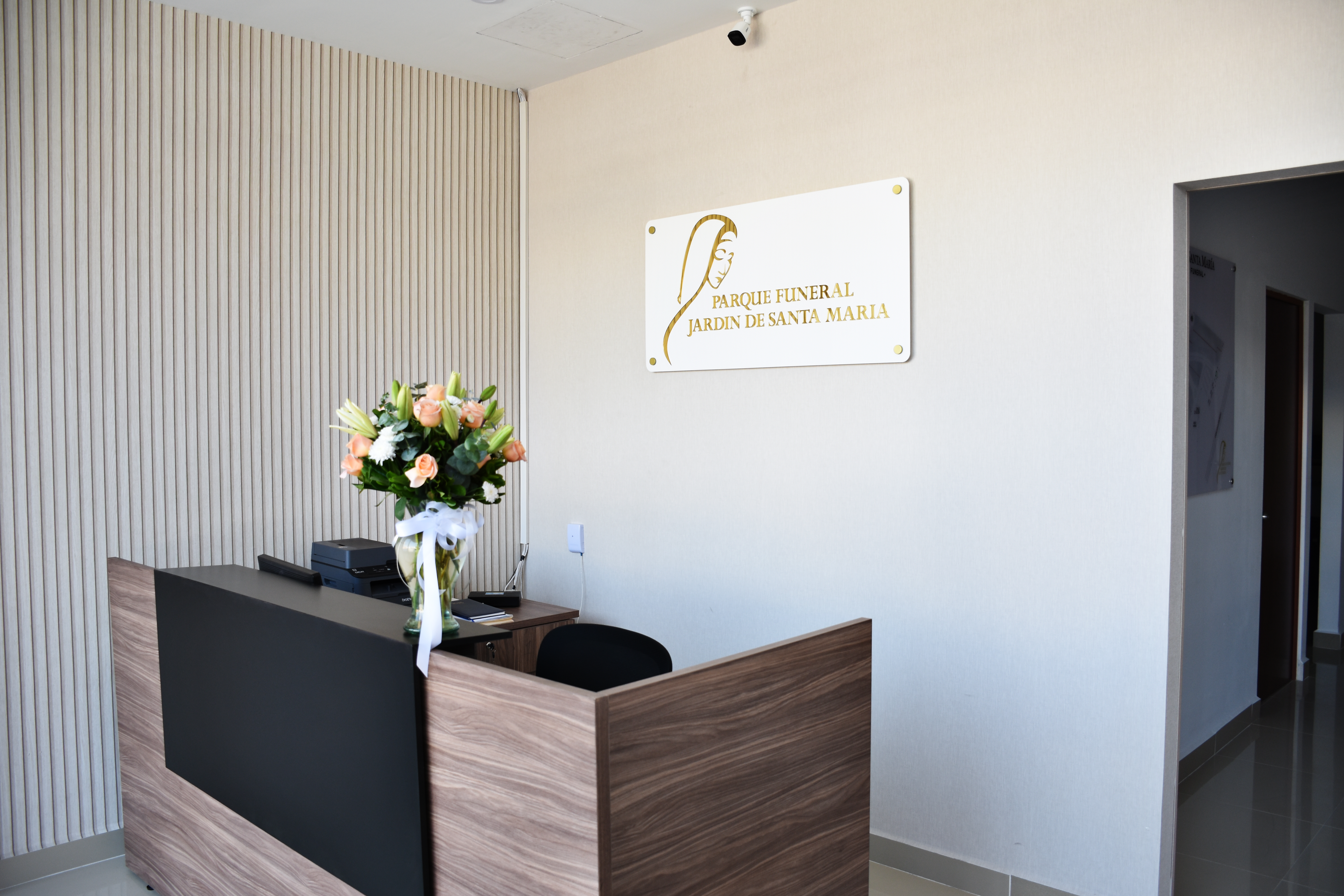 Modern funeral home reception area with wood paneling, floral arrangement, and Parque Funeral Jardim de Santa Maria sign