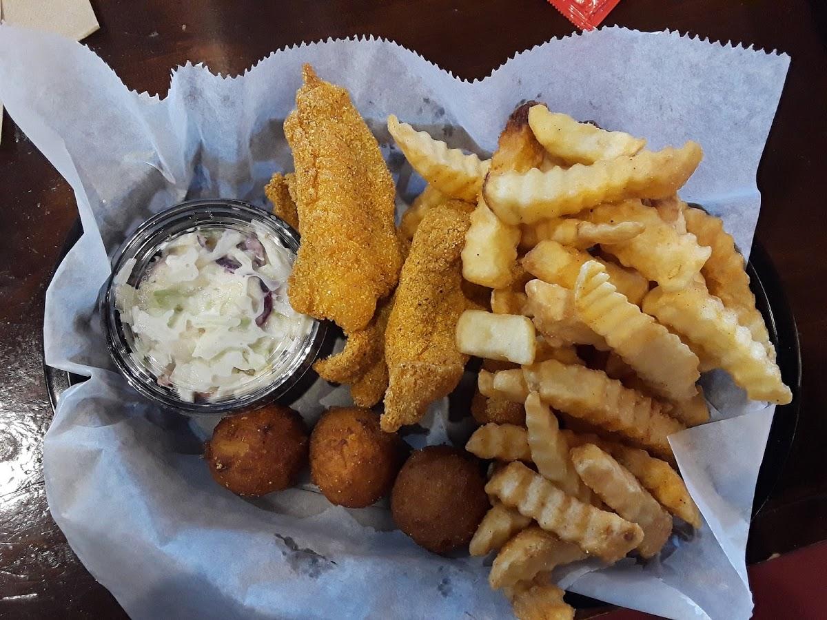 Basket of fried catfish, crinkle-cut fries, coleslaw, and hush puppies on parchment paper.