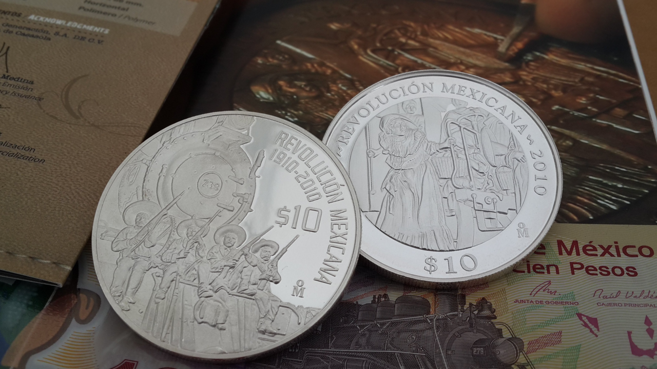 Monedas conmemorativas de la Revolución Mexicana 1910-2010 sobre un billete de cien pesos mexicanos.