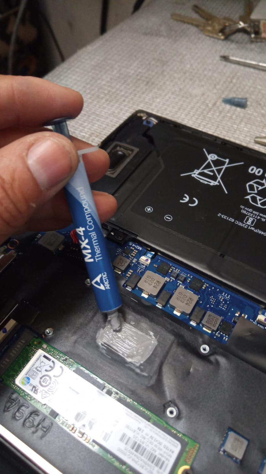 Aplicación de pasta térmica MX-4 en una computadora portátil abierta, junto a la memoria RAM y otros componentes electrónicos.