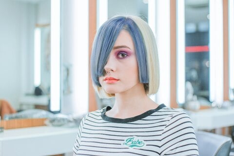 Mujer con peinado bob y mechones azulados en un salón de belleza moderno.