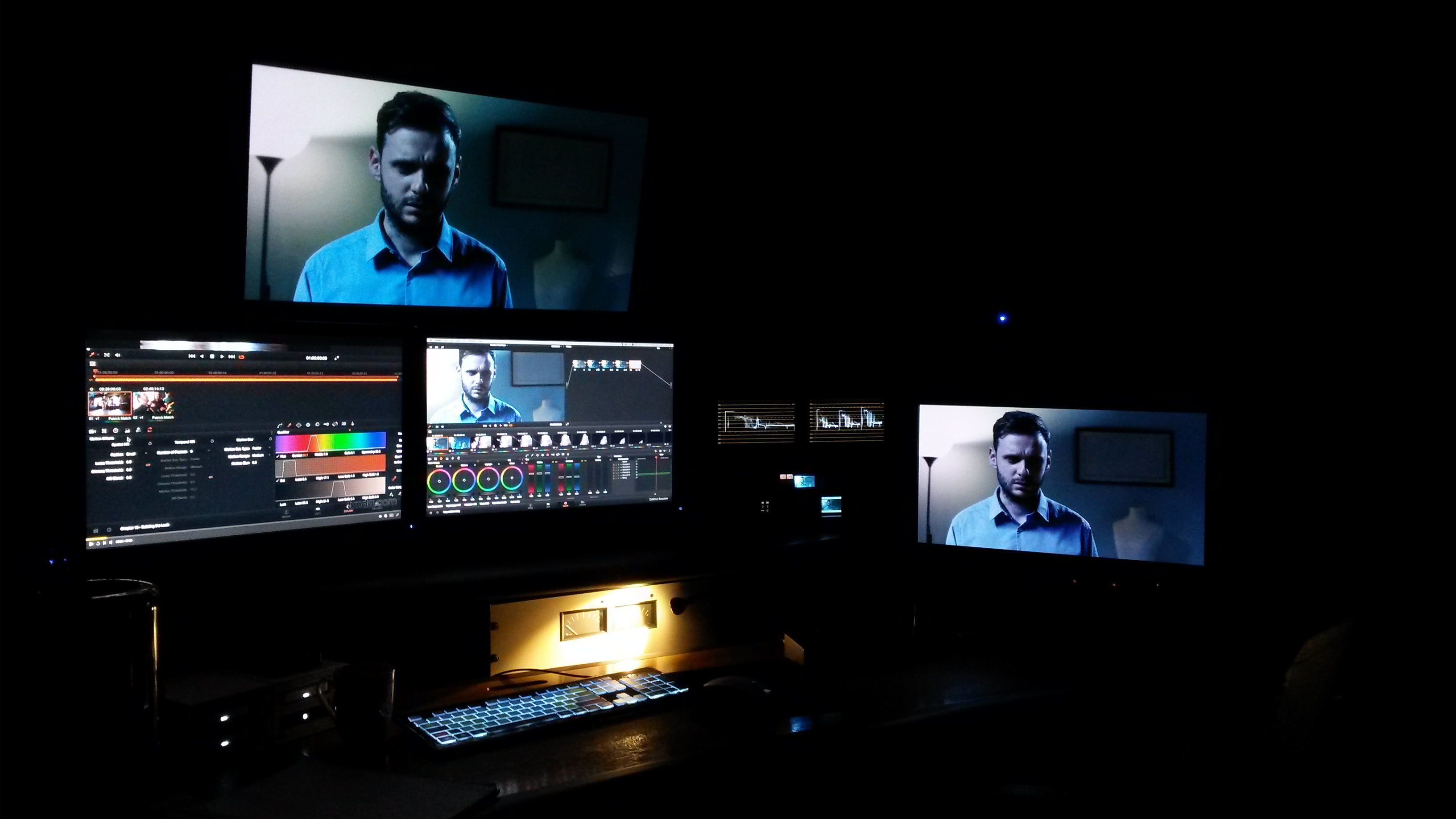 Dark video editing suite with multiple monitors showing color grading software and a man on screen