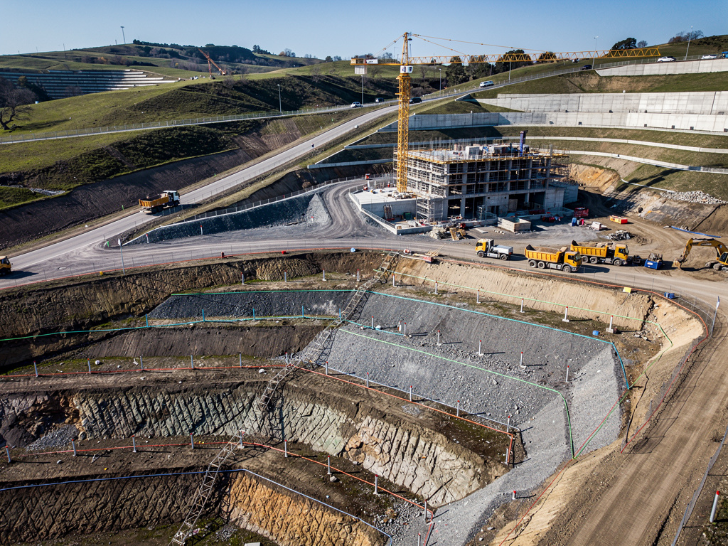 Vista aérea de obra de construcción con grúa, edificio en construcción, camiones y excavación en zona rural