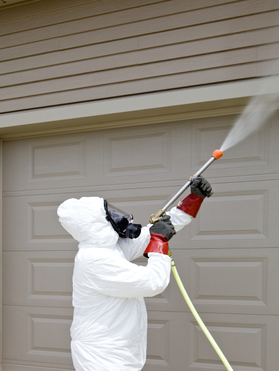 Pest control worker spraying insecticide on a home’s garage 