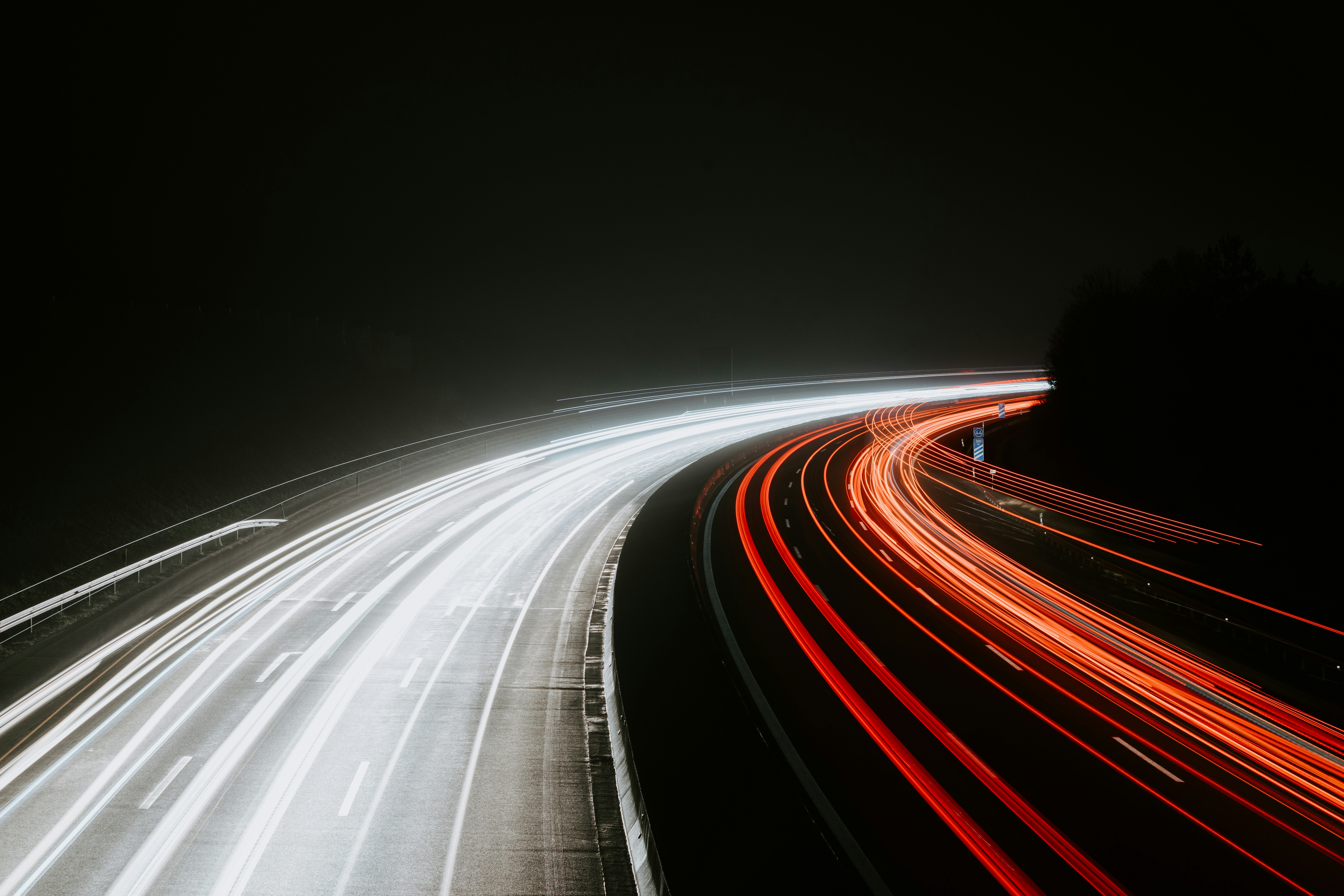 Tráfico nocturno con luces rojas y blancas en movimiento en una carretera oscura.
