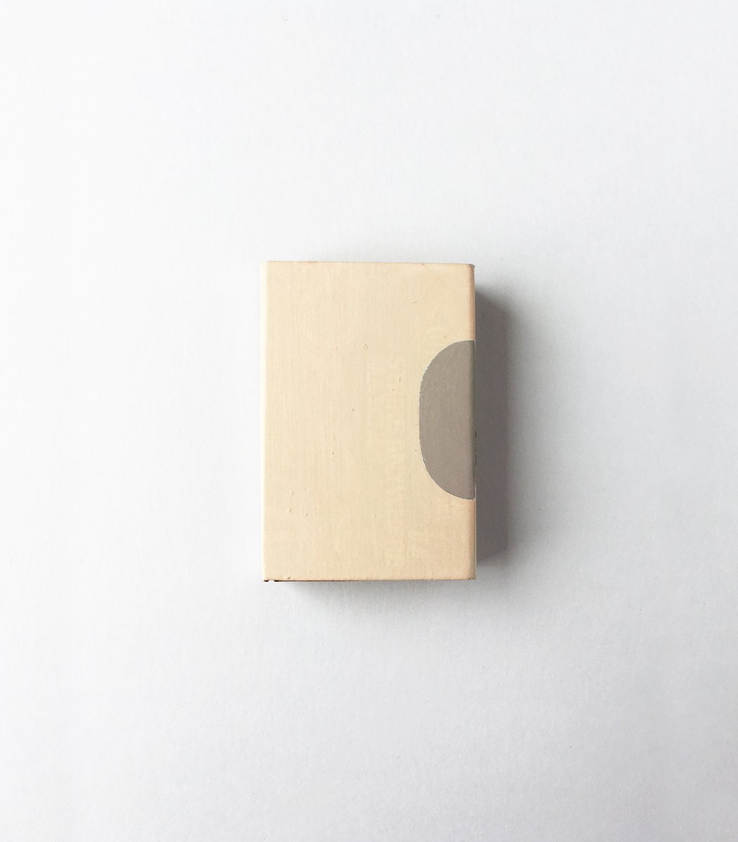 A matchbox with a bisected oval painted on one edge in taupe on cream.