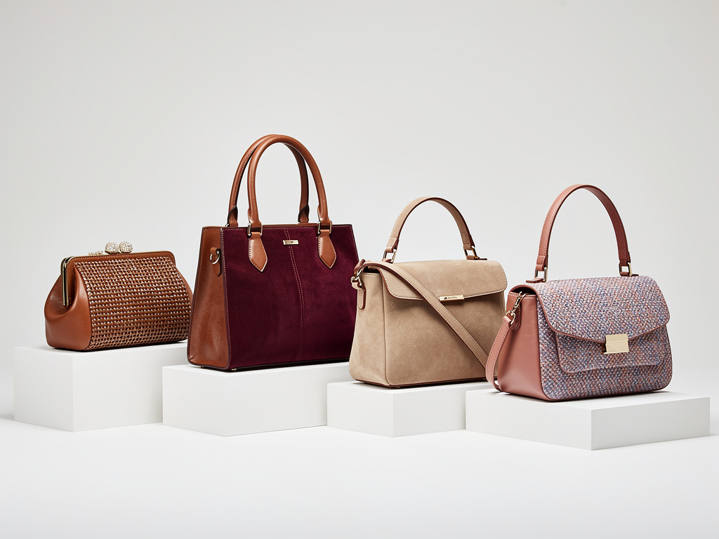 Four stylish women's handbags displayed on white pedestals, including leather, suede, woven, and patterned designs Four stylish women's handbags displayed on white pedestals, including leather, suede, woven, and patterned designs