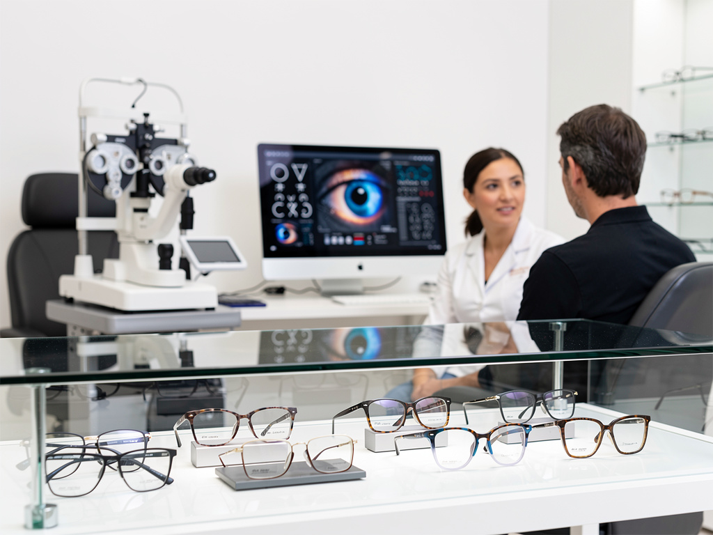 Consulta en óptica con optometrista, paciente, equipo oftalmológico y gafas en exhibición