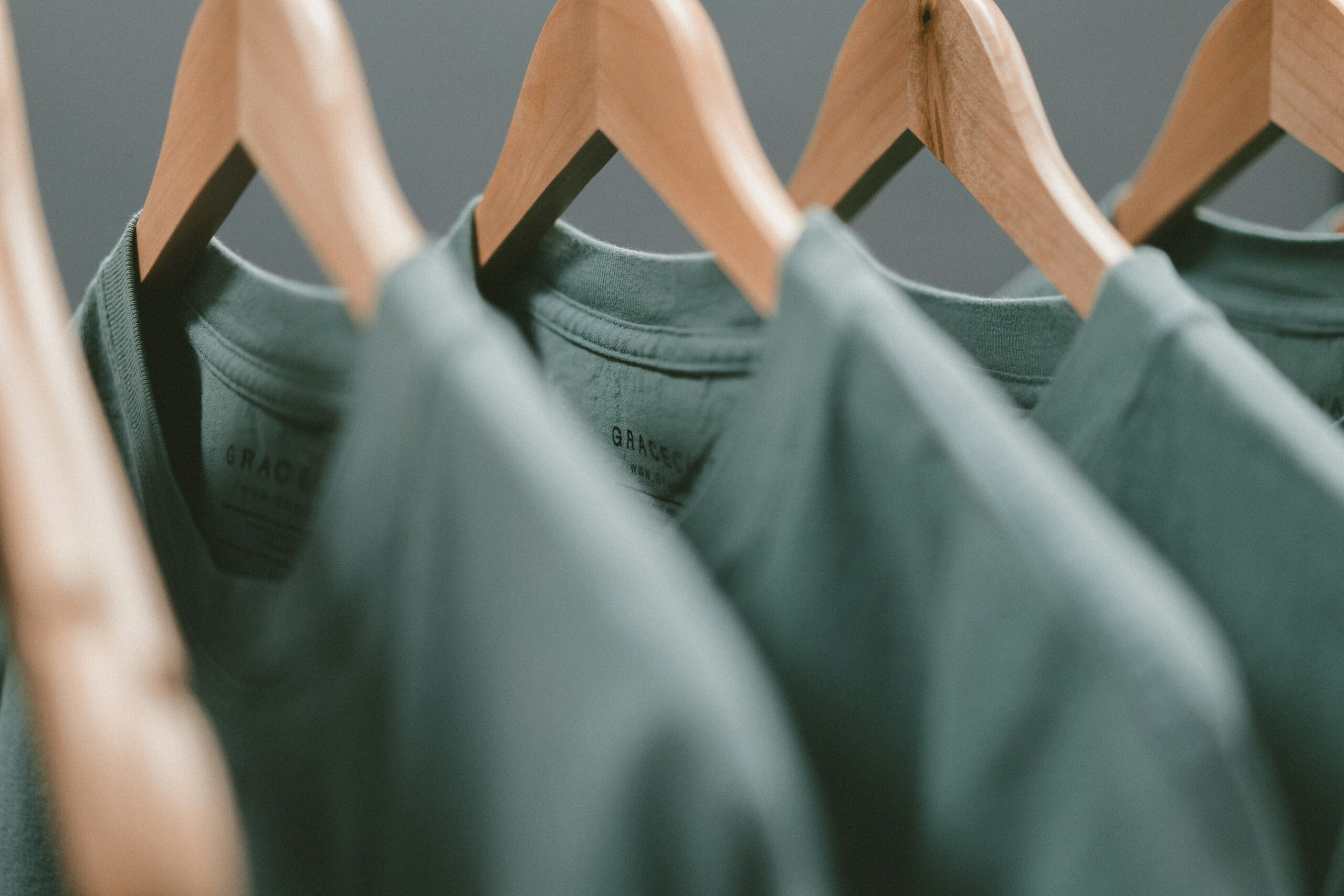 Camisetas verdes colgadas en perchas de madera.