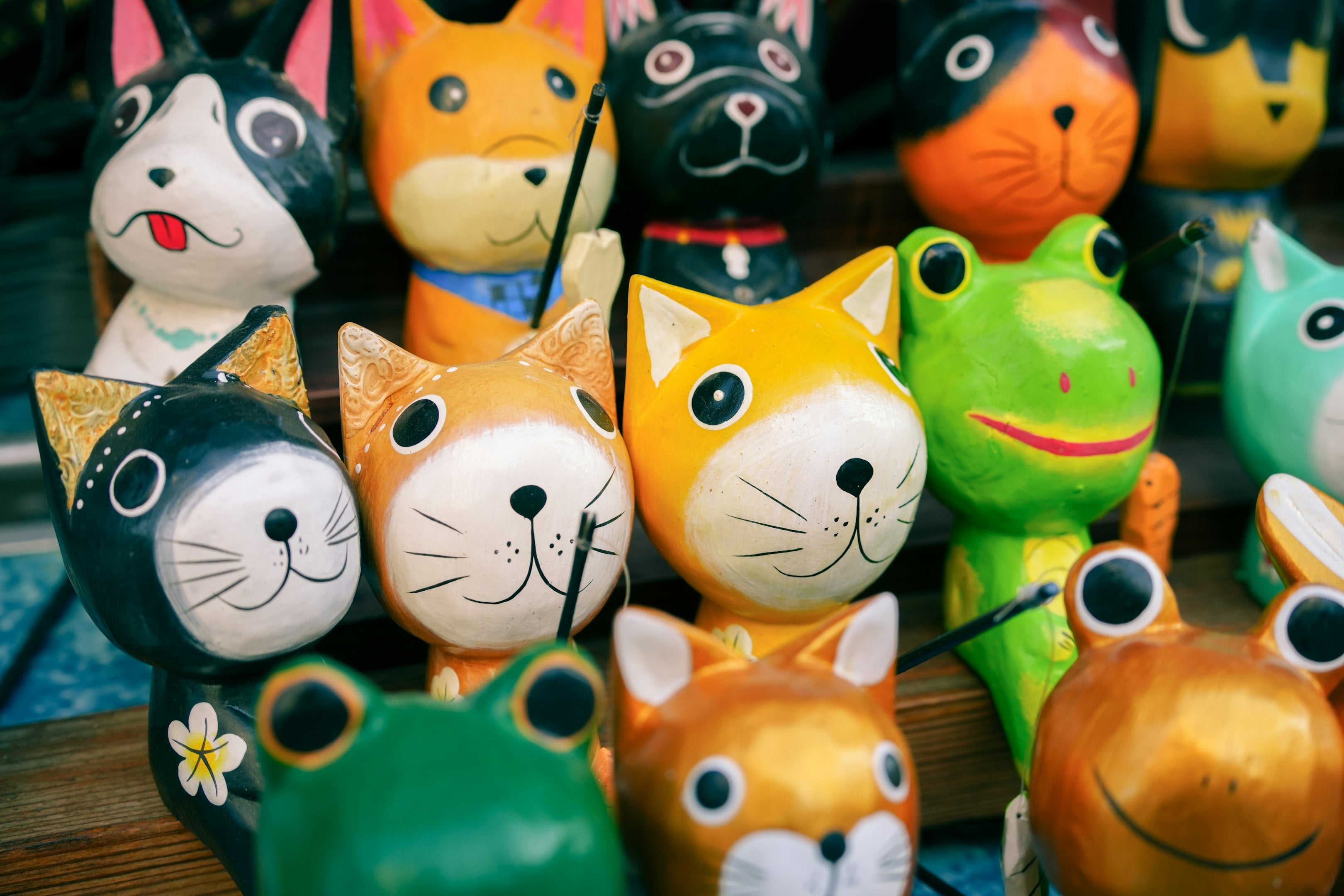 Colorful handmade animal figurines, including cats and frogs, displayed on a wooden shelf. Colorful handmade animal figurines, including cats and frogs, displayed on a wooden shelf.