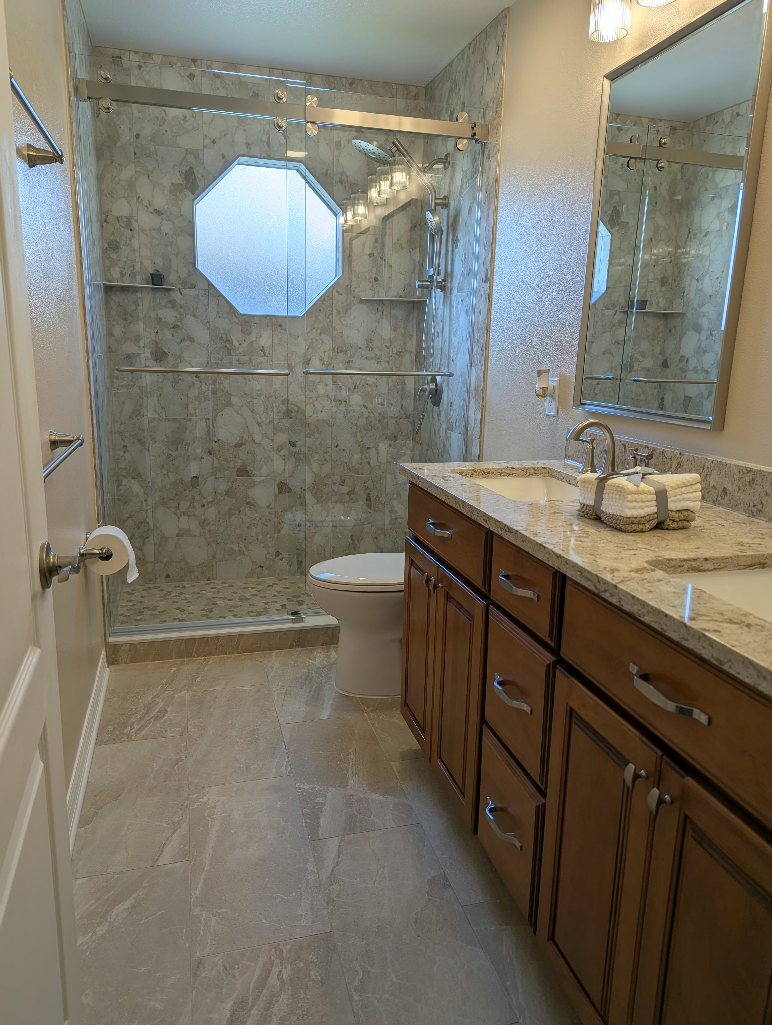 Inviting bathroom showcasing a beautiful window focal point, featuring 12x24 matte porcelain
floor tiles and polished 12x24 shower wall tiles, completed with a brush-nickel bypassing barn-style door.