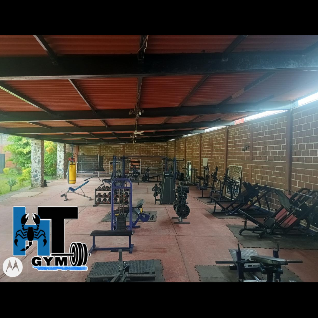 Mujer en ropa deportiva sonriendo en un gimnasio moderno con máquinas de ejercicio de fondo.