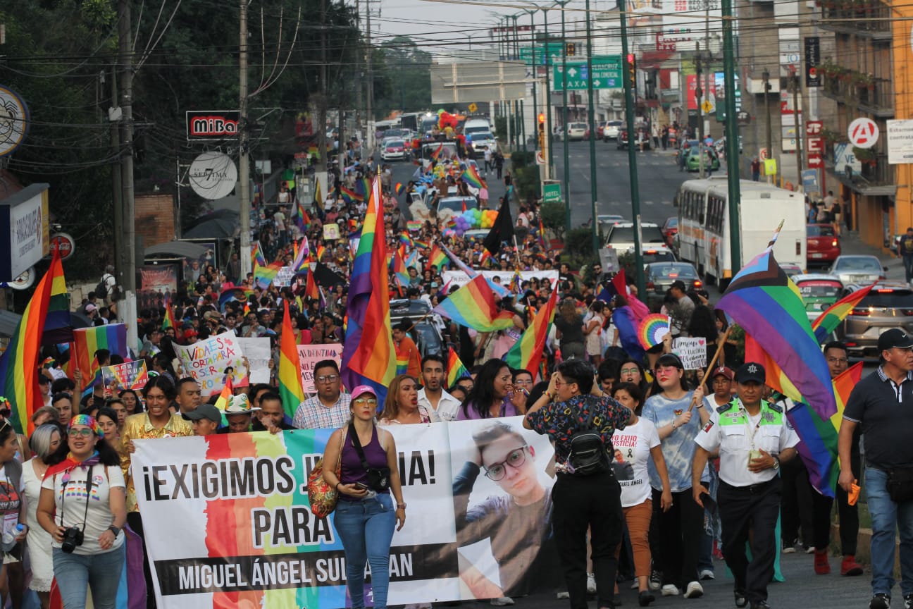 Manifestación LGBTQ+ en una calle, con participantes portando banderas del orgullo y pancartas.