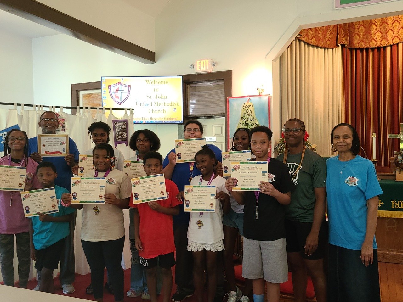 Group of children and adults holding certificates at St. John United Methodist Church event.