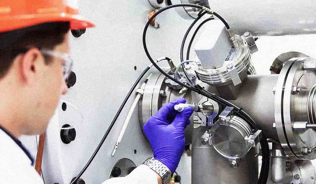 Oficina moderna con empleados trabajando en mesas, rodeados de muebles y estanterías de diseño contemporáneo, con luz natural entrando por amplias ventanas.