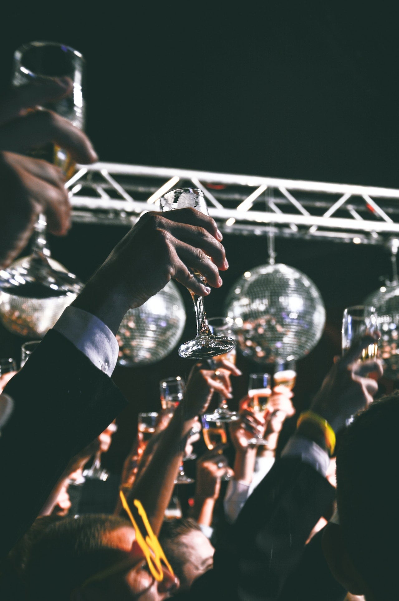 A group of people raising champagne glasses in celebration with disco balls and stage lights in the background.